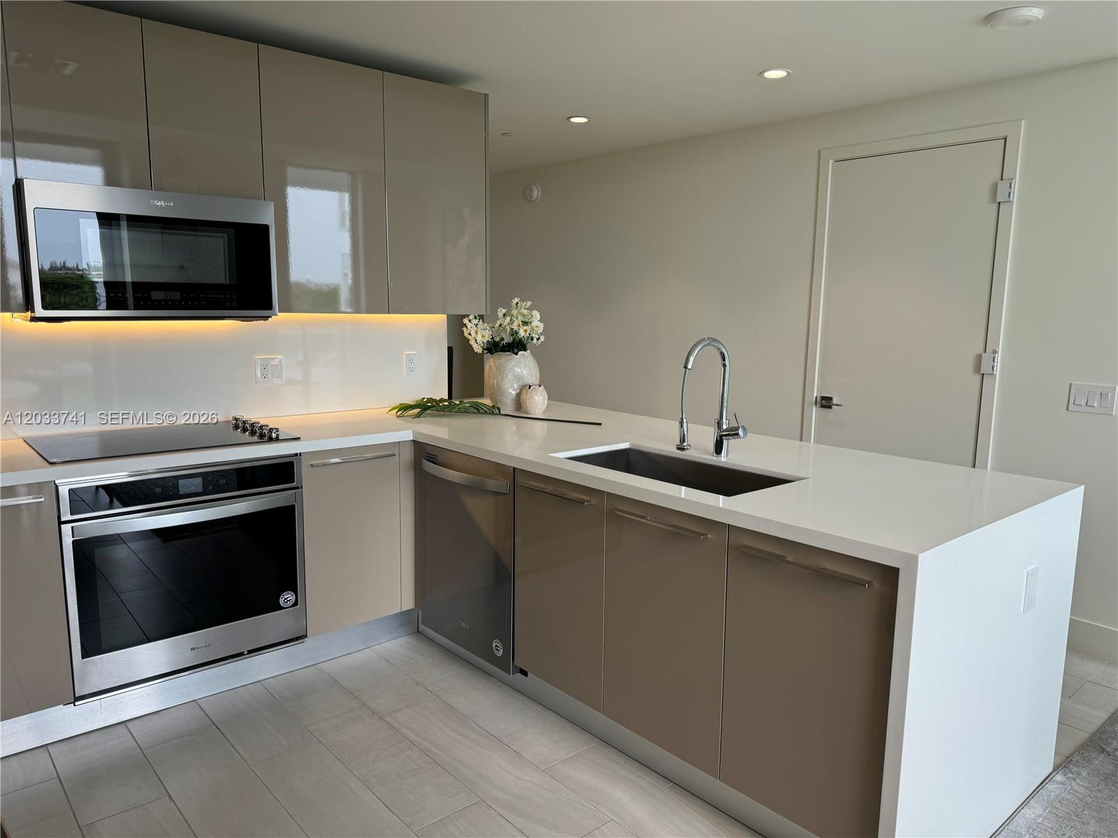 A modern kitchen features taupe flat-panel cabinets, white countertops, stainless steel appliances, and recessed lighting — 2000 Metropica Way # 417, Sunrise FL 33323, SUNRISE, FL