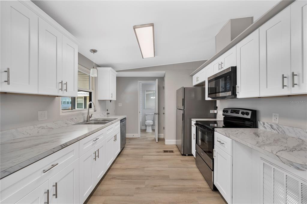 A galley kitchen features white cabinets, marble-look countertops, stainless steel appliances, and light wood flooring — 2055 S FLORAL AVENUE UNIT 117, BARTOW, FL