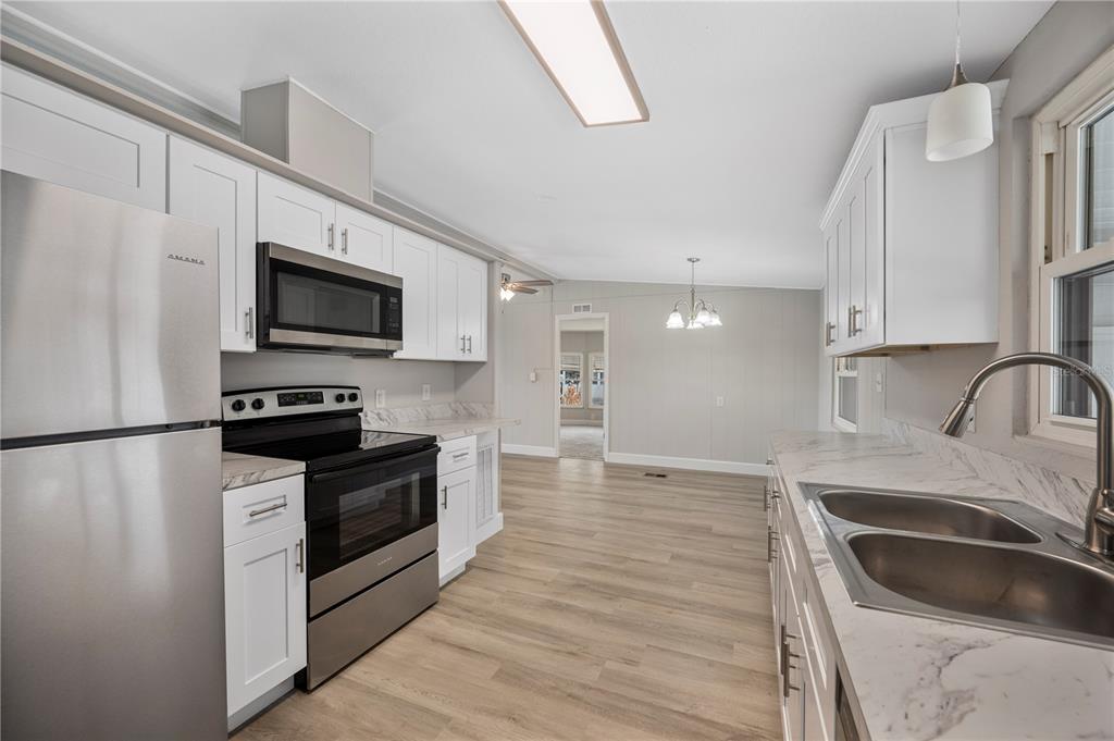 A kitchen features white cabinets, stainless steel appliances, and marble-look countertops with wood-style flooring — 2055 S FLORAL AVENUE UNIT 117, BARTOW, FL