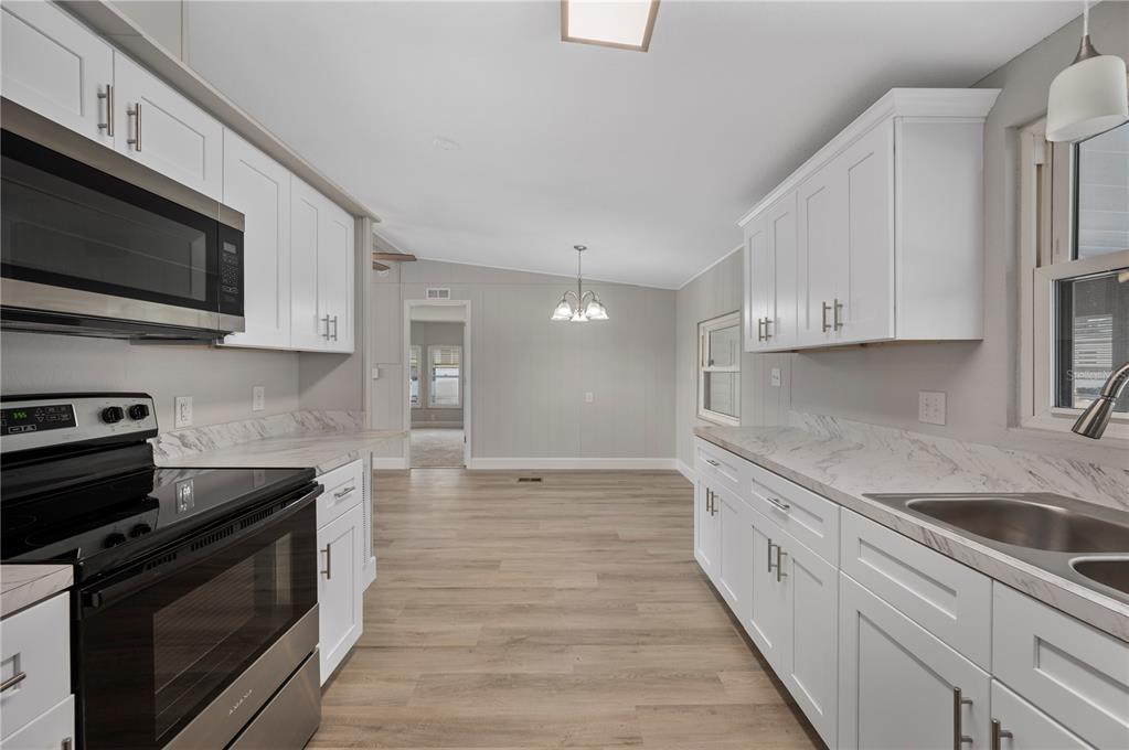 A kitchen with white cabinets, marble-look countertops, and stainless steel appliances leads to a dining area — 2055 S FLORAL AVENUE UNIT 117, BARTOW, FL