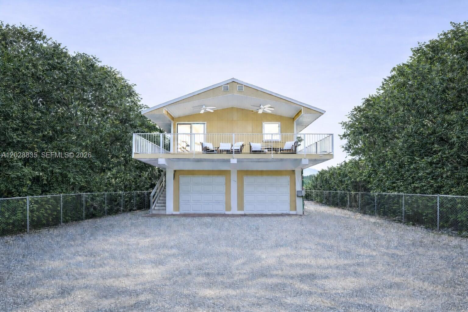 A yellow two-story house with a raised living level, balcony, and two ground-floor garage doors — 335 Bay View Ave, Key Largo FL 33037, KEY LARGO, FL