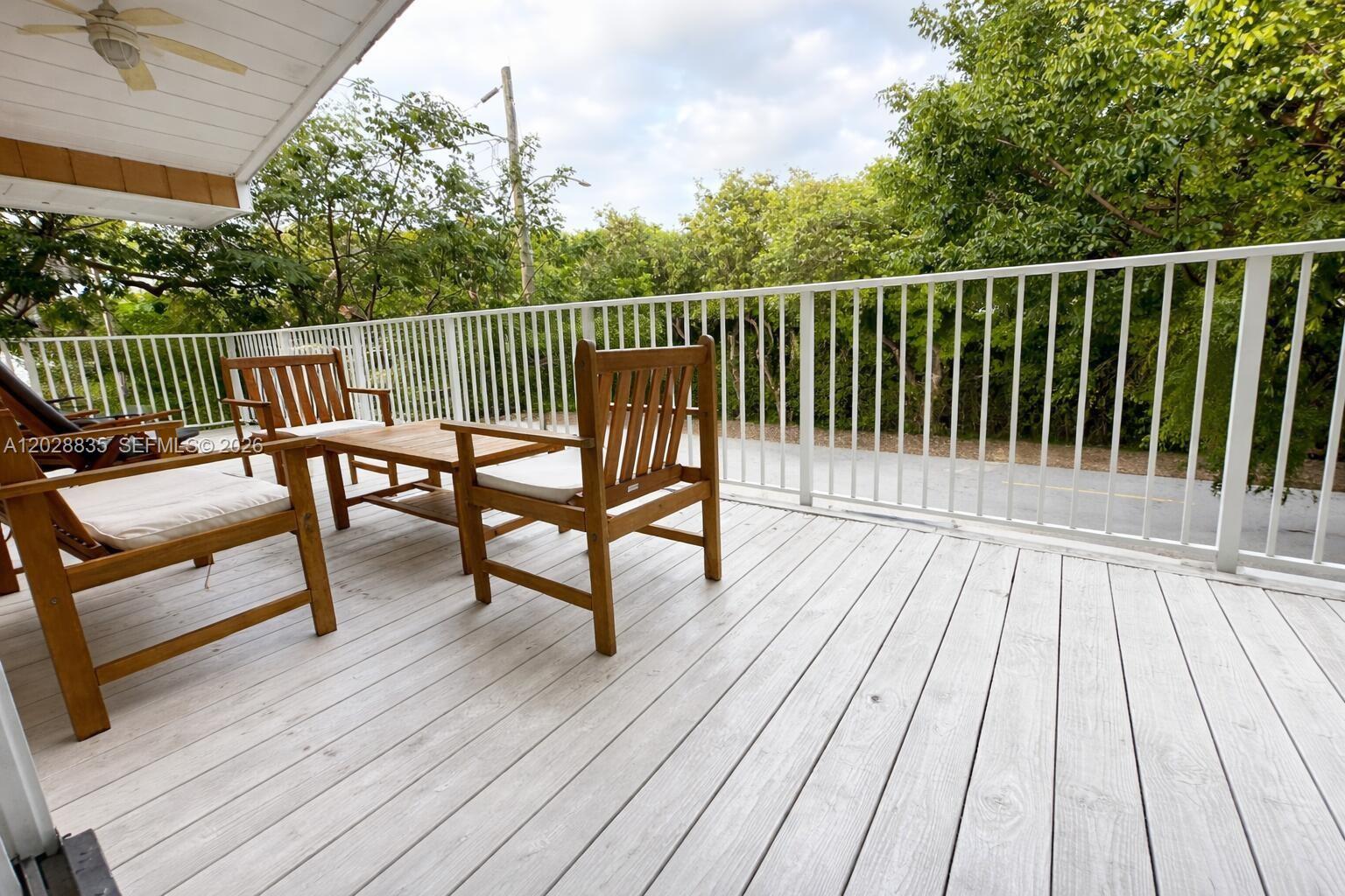 A wooden deck features patio furniture and a white railing overlooking trees and a road — 335 Bay View Ave, Key Largo FL 33037, KEY LARGO, FL
