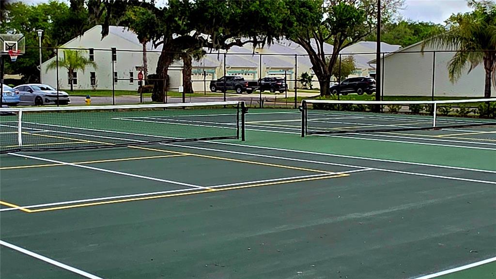 A view of a green tennis court with a net and surrounding chain-link fencing — 2271 CANDLEWOOD LANE, NEW SMYRNA BEACH, FL