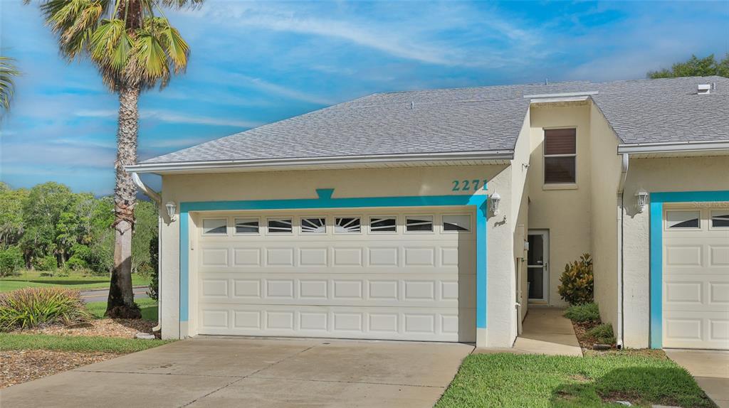 A beige single-story townhouse with a two-car garage and a blue-trimmed entryway — 2271 CANDLEWOOD LANE, NEW SMYRNA BEACH, FL