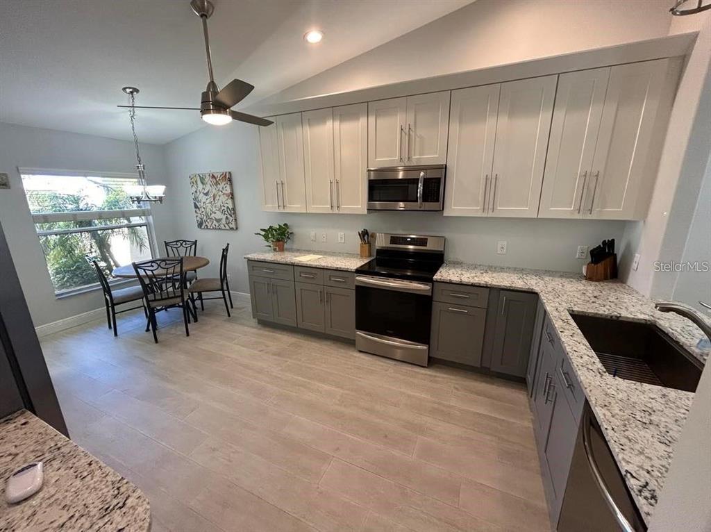 A kitchen with gray lower cabinets, white upper cabinets, granite countertops, and an adjacent dining area — 3701 ALBACETE CIRCLE UNIT 98, PUNTA GORDA, FL