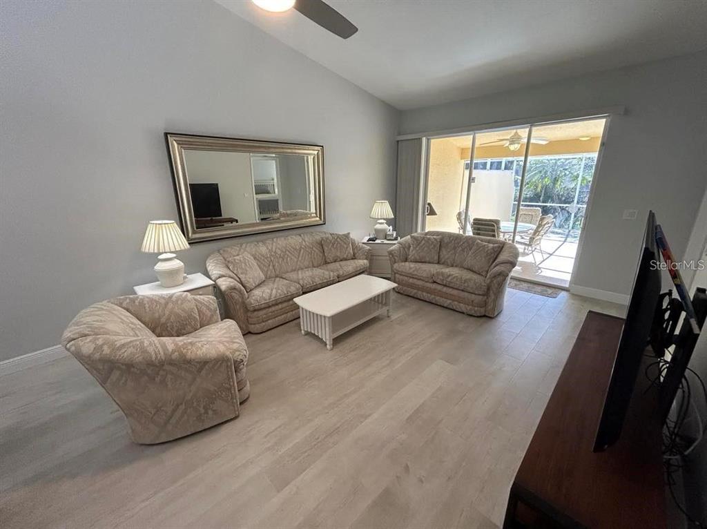 A living room features light wood-look flooring, patterned furniture, a large mirror, and sliding glass doors — 3701 ALBACETE CIRCLE UNIT 98, PUNTA GORDA, FL