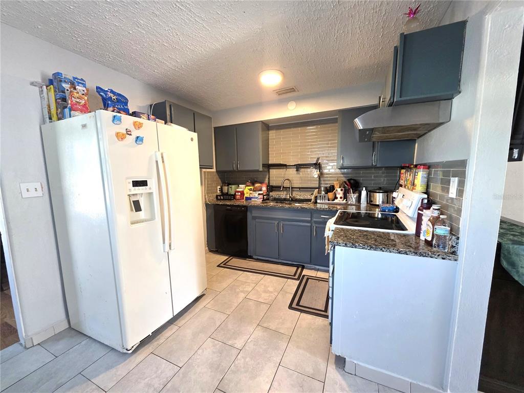 A kitchen features gray cabinets, granite countertops, a white refrigerator, and light-colored tile flooring — 2137 4TH STREET E, BRADENTON, FL
