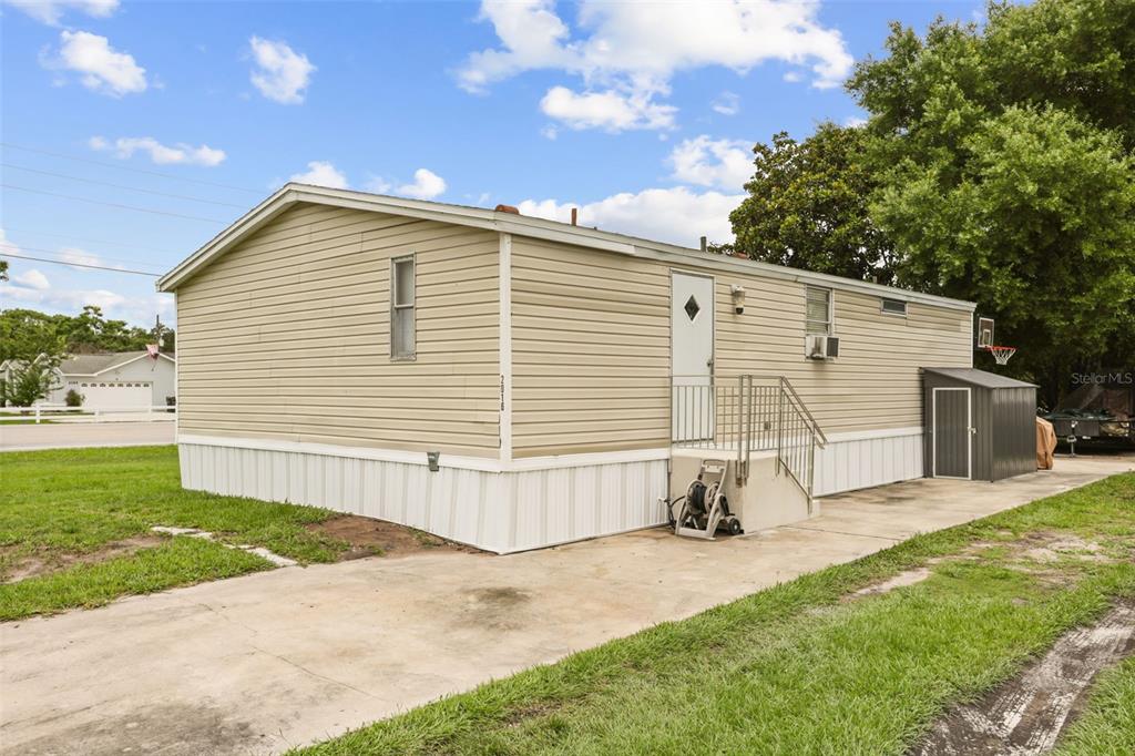 A tan mobile home with a concrete driveway, metal stairs, and a small storage shed — 2016 OAK STREET, ST CLOUD, FL