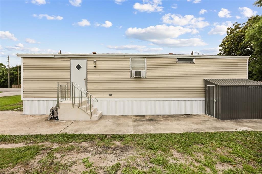 A beige mobile home exterior features a white door, stairs, and an attached metal shed — 2016 OAK STREET, ST CLOUD, FL