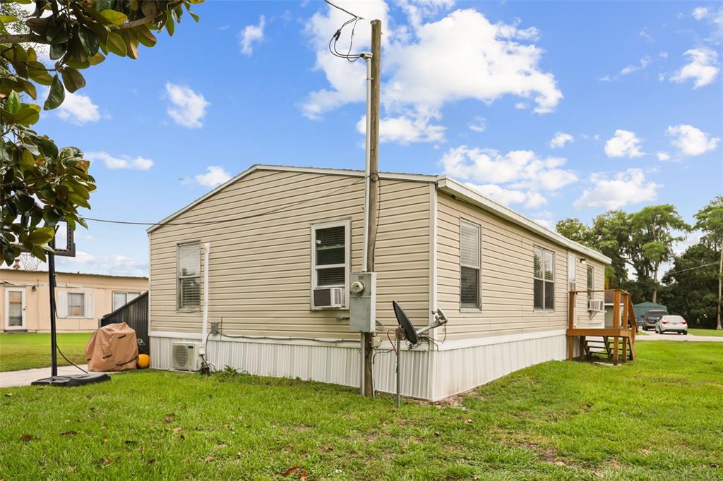 A beige single-wide mobile home sits on a grassy lot under a blue sky — 2016 OAK STREET, ST CLOUD, FL