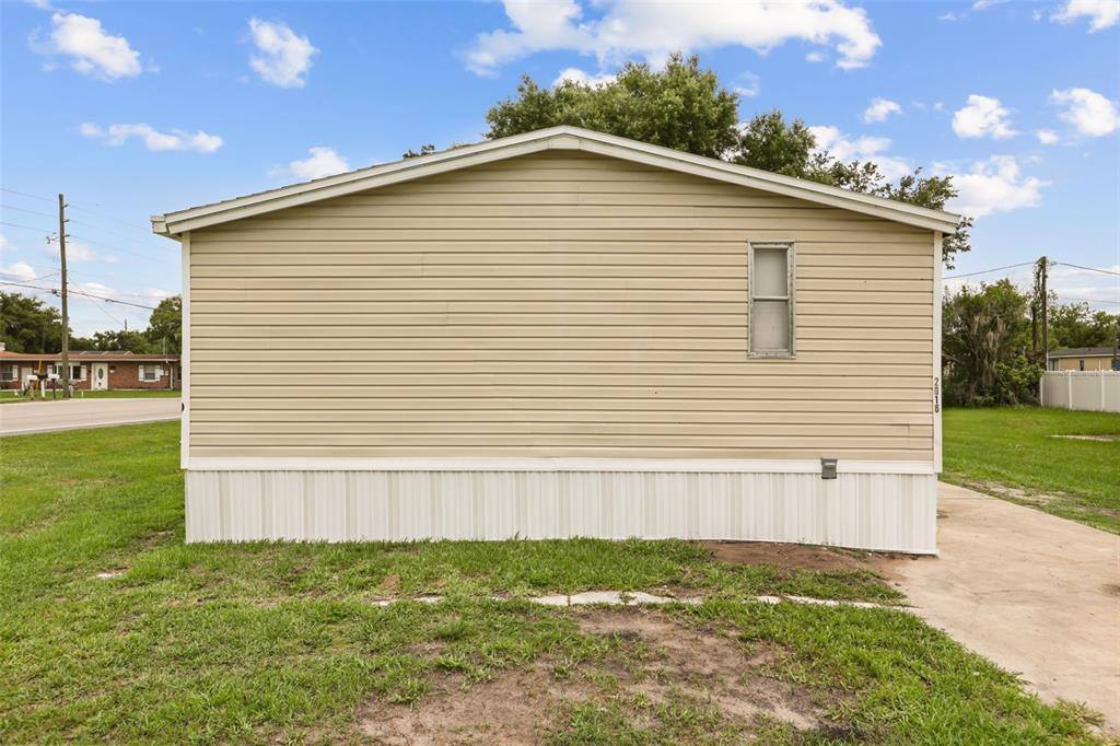 The exterior side view of a tan mobile home with white skirting and one window — 2016 OAK STREET, ST CLOUD, FL