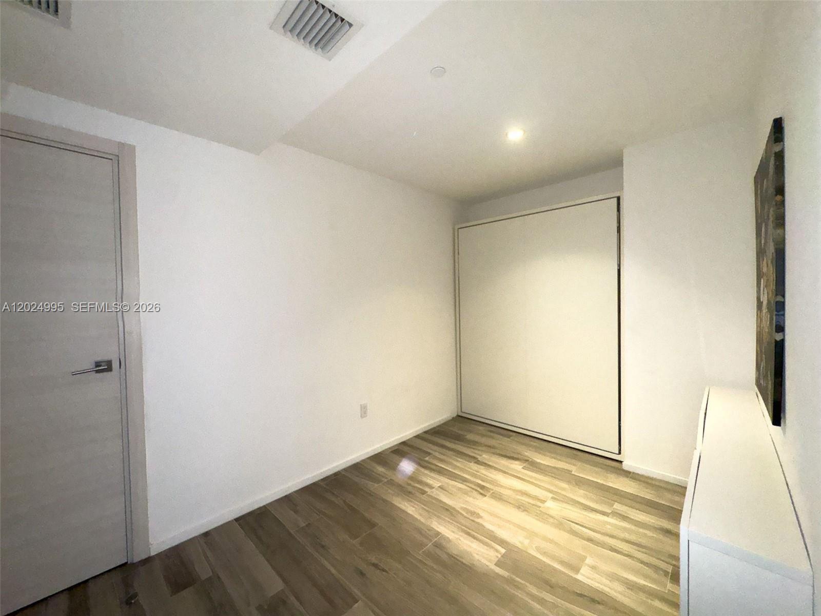 This room features light wood-look flooring, white walls, a closed Murphy bed, and a door — 801 S Miami Ave # 2607, Miami FL 33130, MIAMI, FL