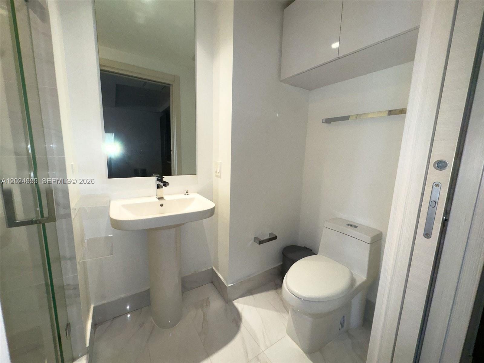 A modern bathroom features a pedestal sink, a toilet, a glass shower, and white cabinetry — 801 S Miami Ave # 2607, Miami FL 33130, MIAMI, FL
