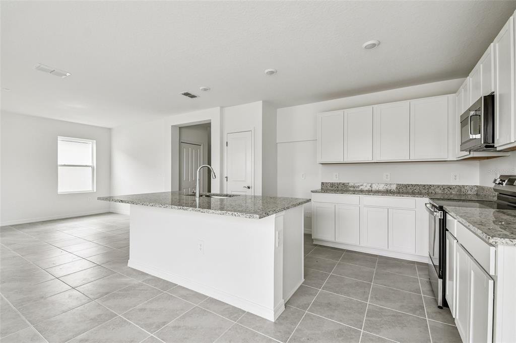 A kitchen with white cabinets, granite countertops, a center island, and gray tile flooring — 9118 OPTIMIST WAY, PALMETTO, FL