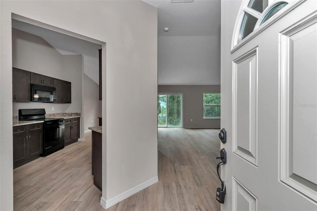 An entryway opens into a kitchen with dark cabinets and a living area with light flooring — 23465 SW COTTONWOOD LANE, DUNNELLON, FL