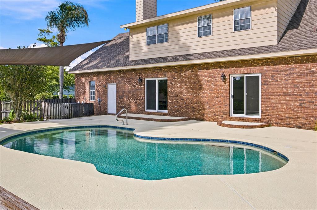 A brick house exterior features a swimming pool and a patio with a shade sail — 3220 SE 21ST AVENUE, OCALA, FL