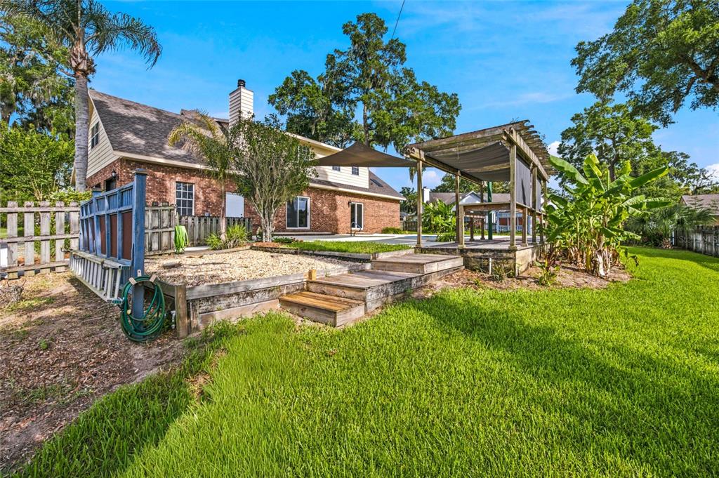 A backyard features a brick house, a wooden pergola, a gravel patio, and a lawn — 3220 SE 21ST AVENUE, OCALA, FL