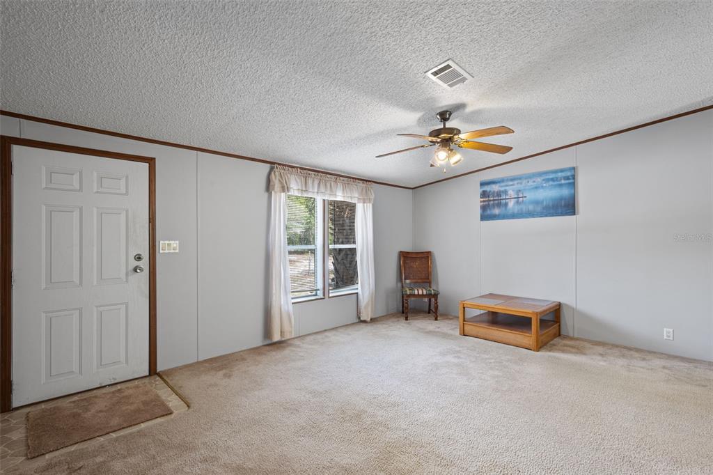 A living room with beige carpet, light gray walls, a ceiling fan, and a front door — 704 SE 791ST STREET, OLD TOWN, FL