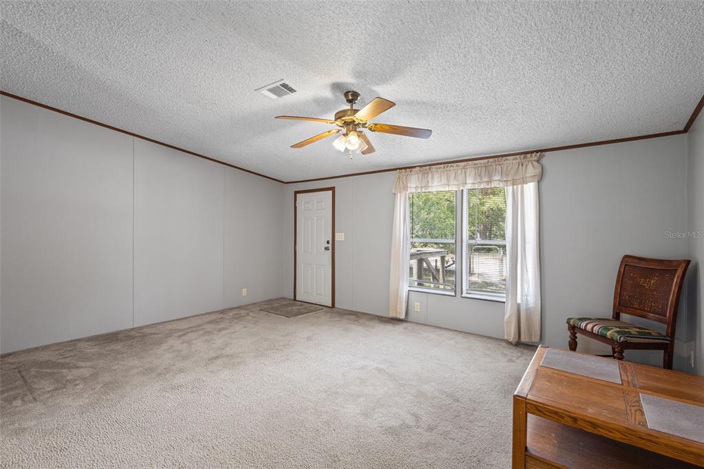 A carpeted living room features a ceiling fan, a white door, and a window with curtains — 704 SE 791ST STREET, OLD TOWN, FL