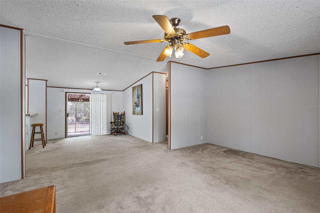 A carpeted living room features white paneled walls, a ceiling fan, and a sliding glass door — 704 SE 791ST STREET, OLD TOWN, FL