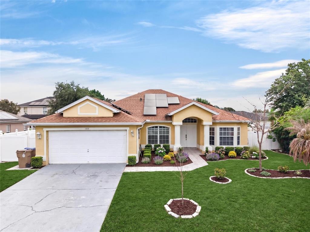 A single-story yellow house with a white garage, solar panels, and a landscaped front yard — 107 BIANCA COURT, KISSIMMEE, FL