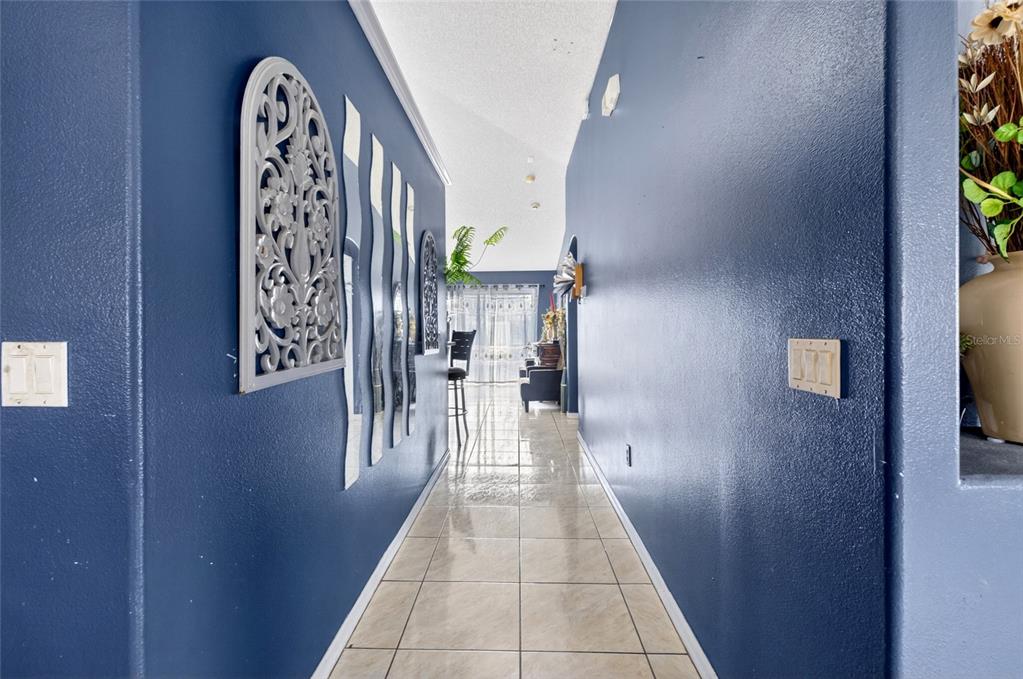 A hallway with blue walls, tiled floors, and decorative wall art leads toward a living area — 107 BIANCA COURT, KISSIMMEE, FL