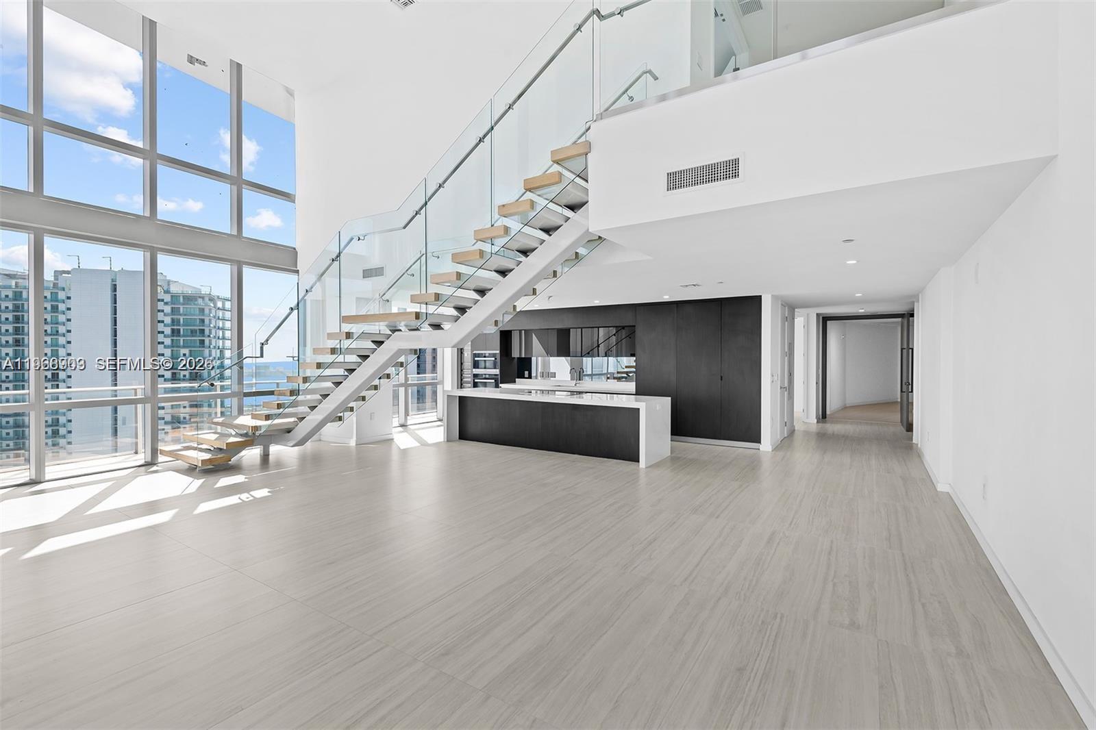 A modern, open-concept living area features a floating staircase, floor-to-ceiling windows, and a kitchen island — 851 NE 1st Ave # 5001, Miami FL 33132, MIAMI, FL
