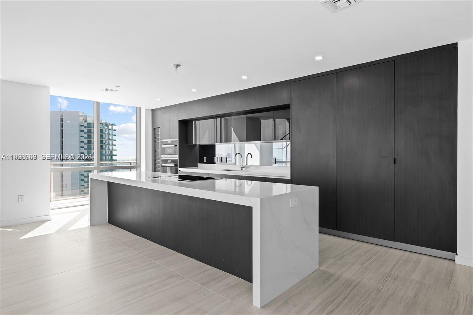 A modern kitchen features dark wood cabinetry, a white waterfall island, and floor-to-ceiling windows — 851 NE 1st Ave # 5001, Miami FL 33132, MIAMI, FL