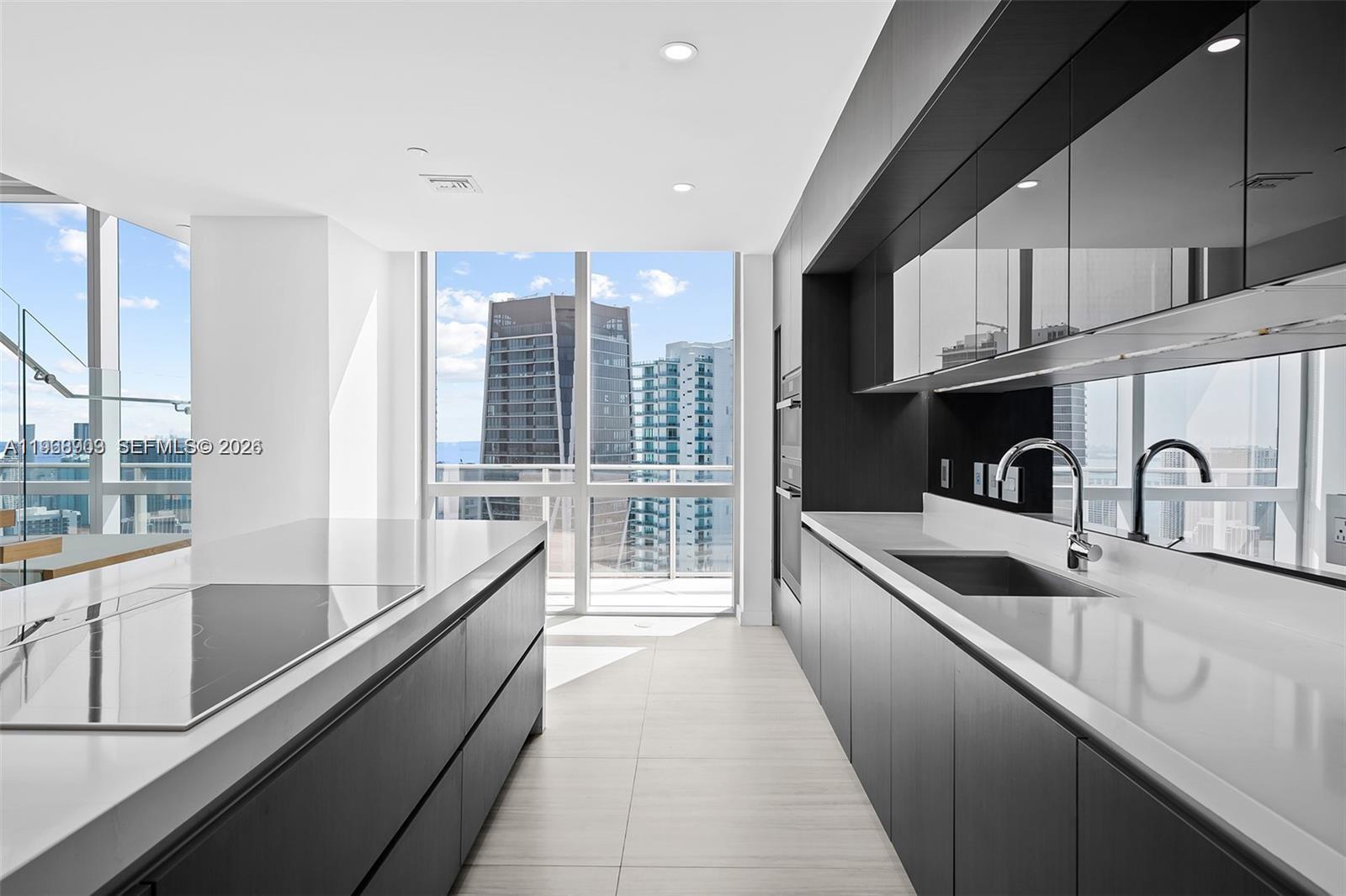 A modern kitchen features dark cabinetry, white countertops, and floor-to-ceiling windows with city views — 851 NE 1st Ave # 5001, Miami FL 33132, MIAMI, FL