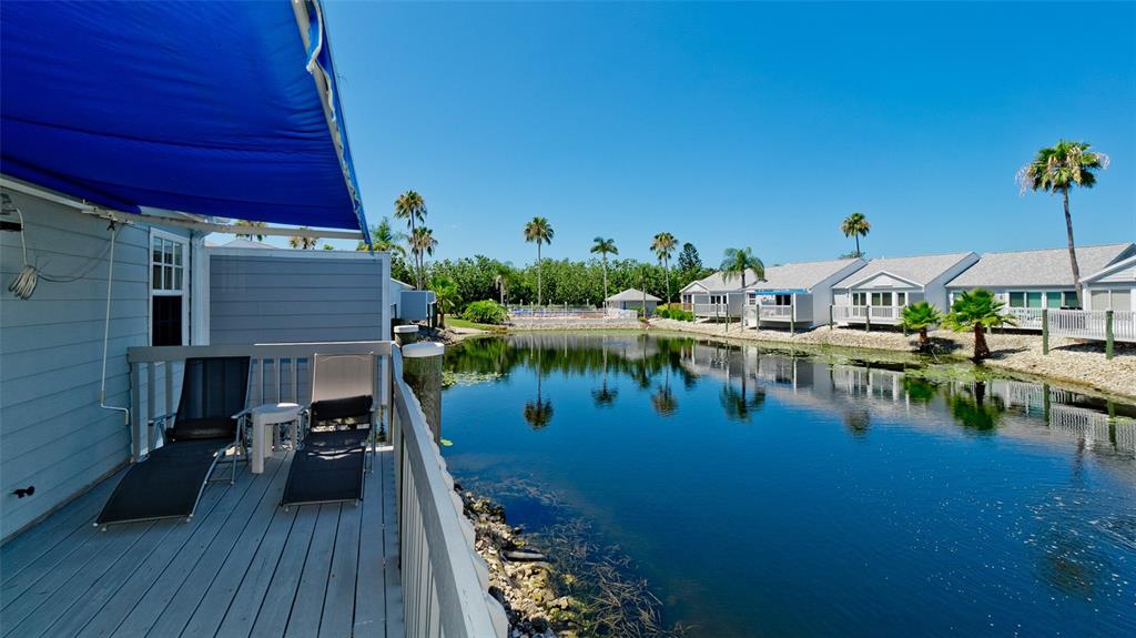 A wooden deck with lounge chairs overlooks a pond surrounded by houses and palm trees — 506 WOODSTORK CIRCLE, BRADENTON, FL
