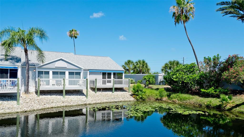 A light-colored house with a screened porch sits beside a pond with lily pads — 506 WOODSTORK CIRCLE, BRADENTON, FL