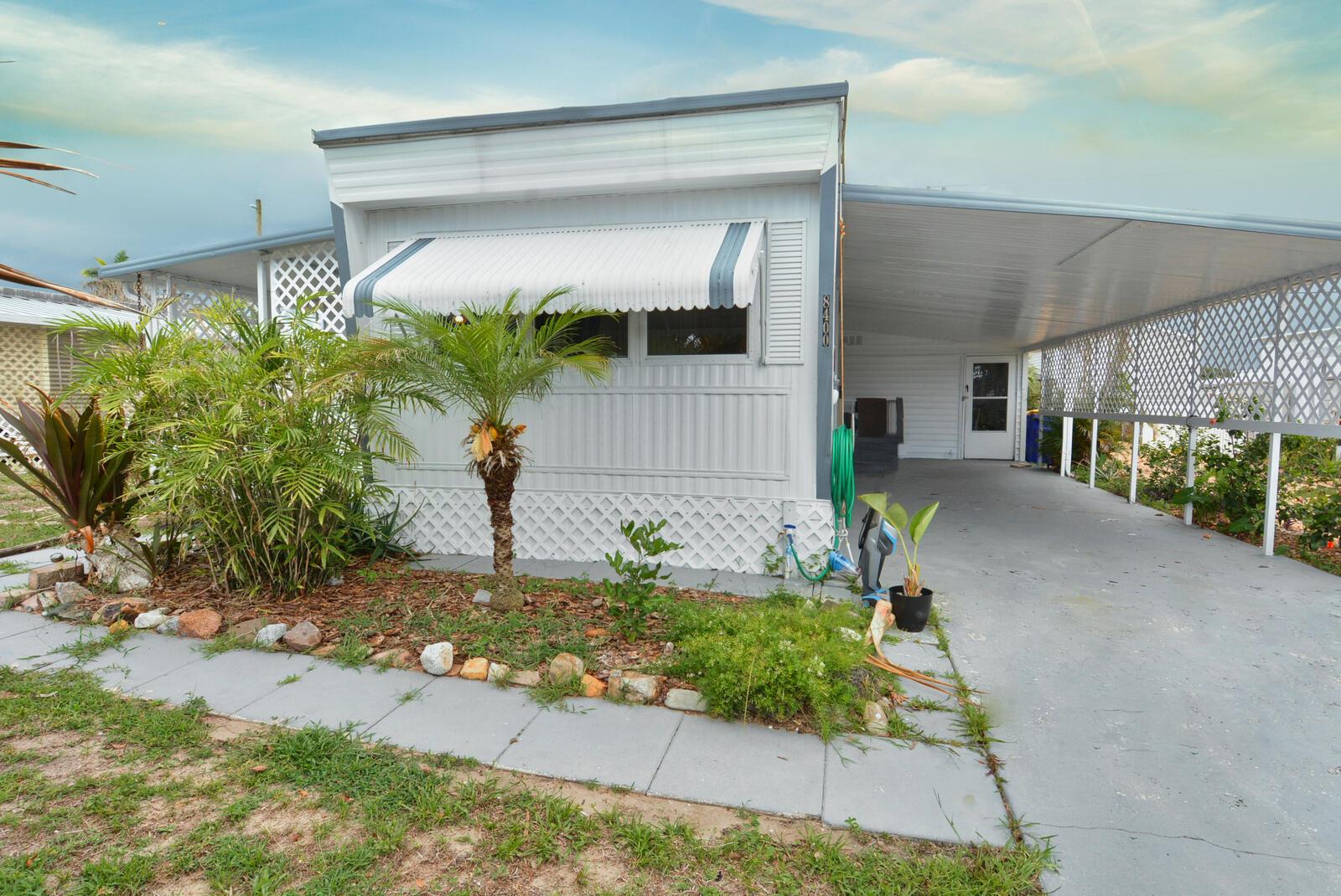 A single-story mobile home with a carport, white siding, and a small front garden — 8400 SE Eagle Avenue, Hobe Sound FL 33455, HOBE SOUND, FL