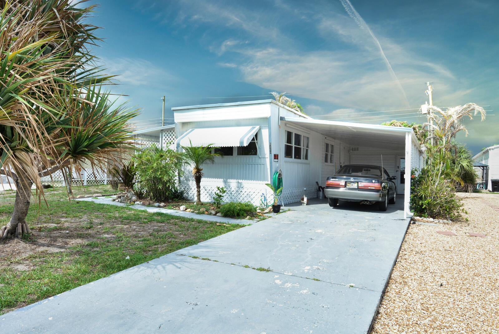 A white mobile home with a carport and a parked car sits on a lot — 8400 SE Eagle Avenue, Hobe Sound FL 33455, HOBE SOUND, FL