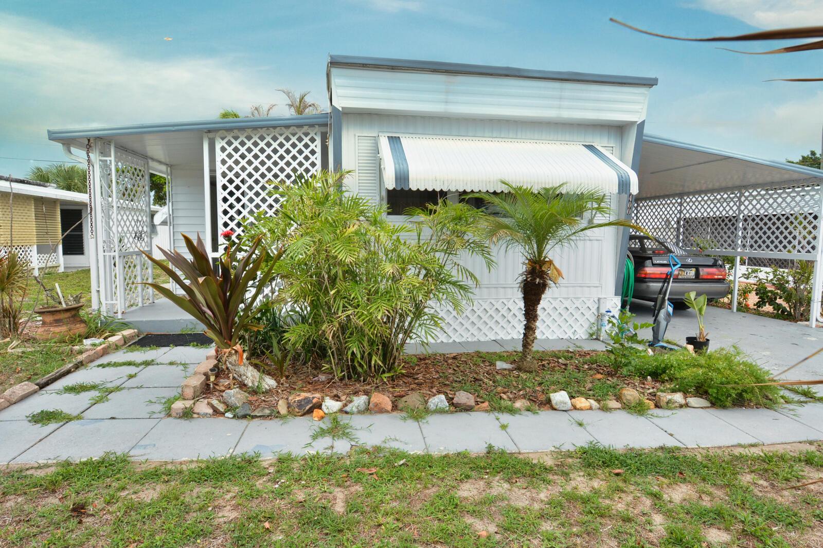A single-story manufactured home with a front porch, carport, and a landscaped garden bed — 8400 SE Eagle Avenue, Hobe Sound FL 33455, HOBE SOUND, FL