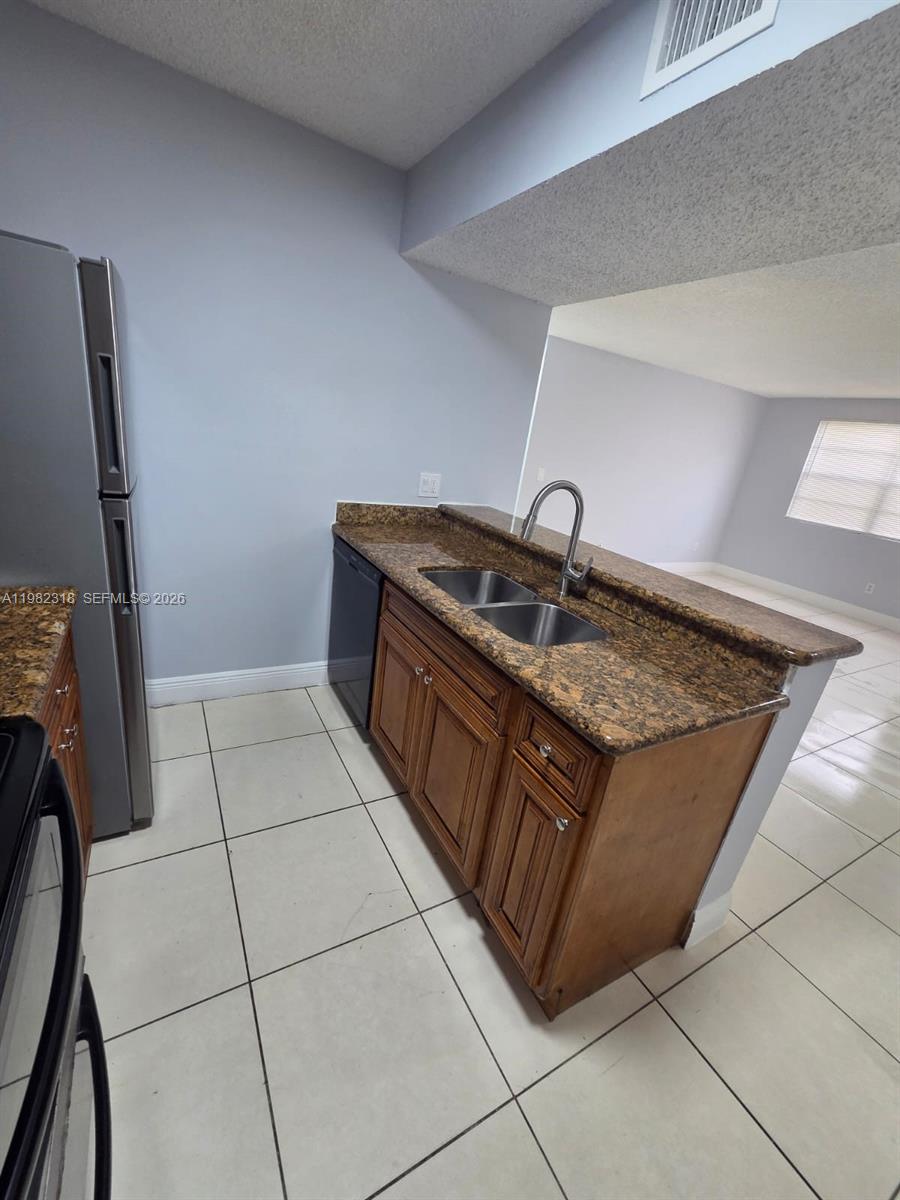 A kitchen features brown wooden cabinets, granite countertops, a double sink, and tile flooring — 1241 SW 46th Ave # 1006, Pompano Beach FL 33069, POMPANO BEACH, FL