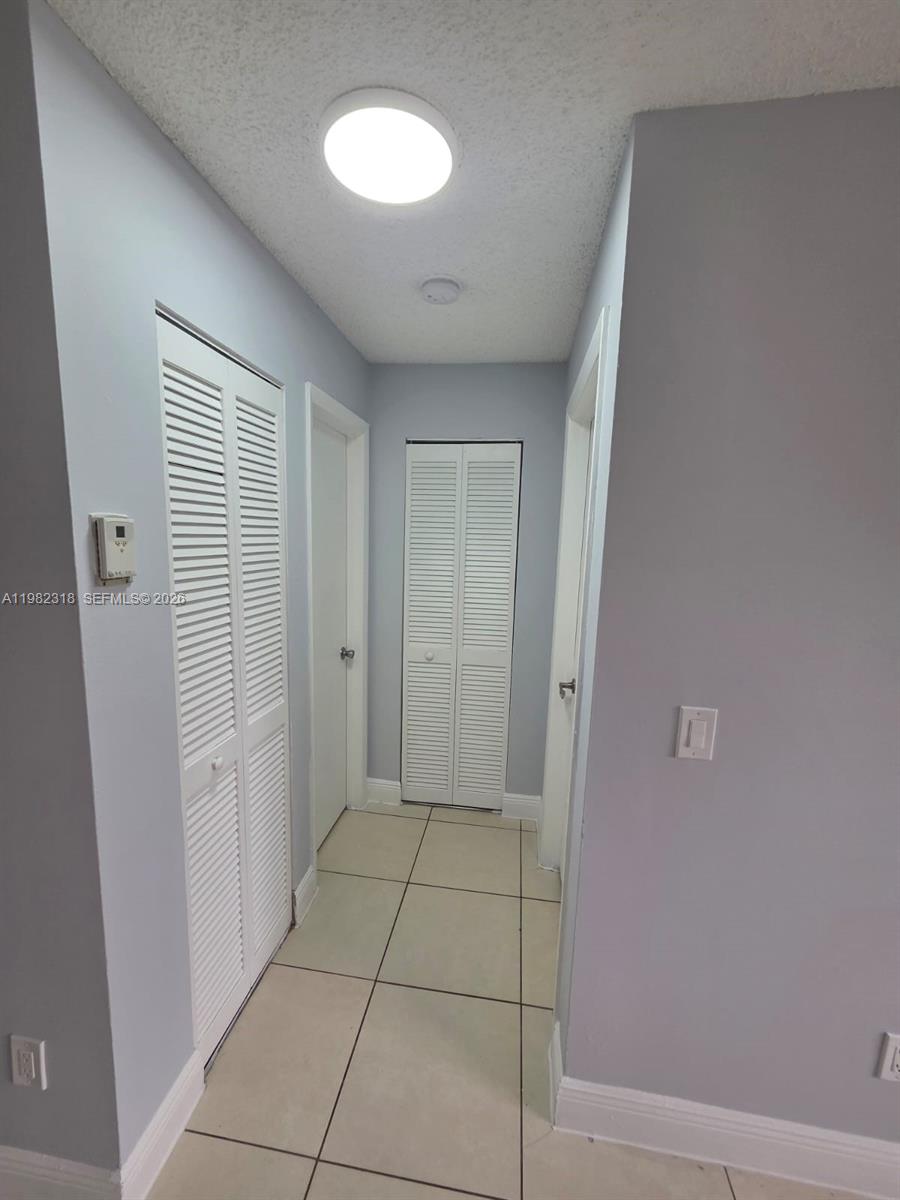 A hallway with light-colored tile flooring, gray walls, and multiple white louvered closet doors — 1241 SW 46th Ave # 1006, Pompano Beach FL 33069, POMPANO BEACH, FL