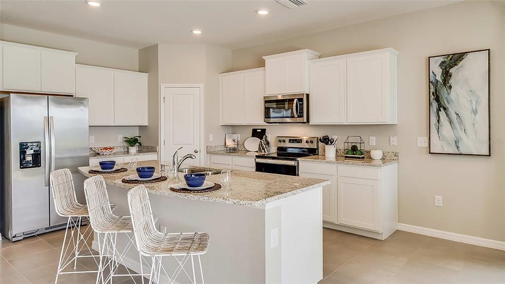 A modern kitchen features white cabinets, granite countertops, a stainless steel refrigerator, and a breakfast island — 4321 SILVER BIRCH COURT, PALMETTO, FL