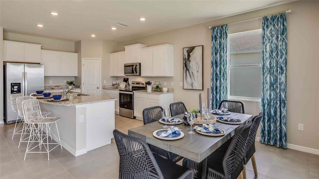 A kitchen with white cabinets and a granite island flows into a dining area — 4321 SILVER BIRCH COURT, PALMETTO, FL