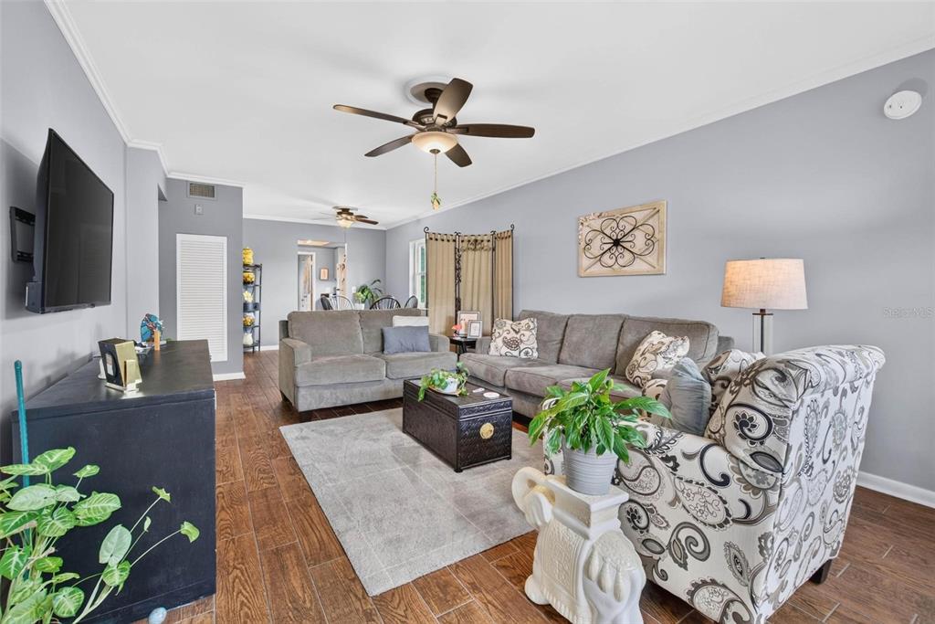 A living room features gray walls, wood-look tile flooring, a gray sofa, and patterned armchairs — 1900 58TH AVENUE N UNIT 14, ST PETERSBURG, FL