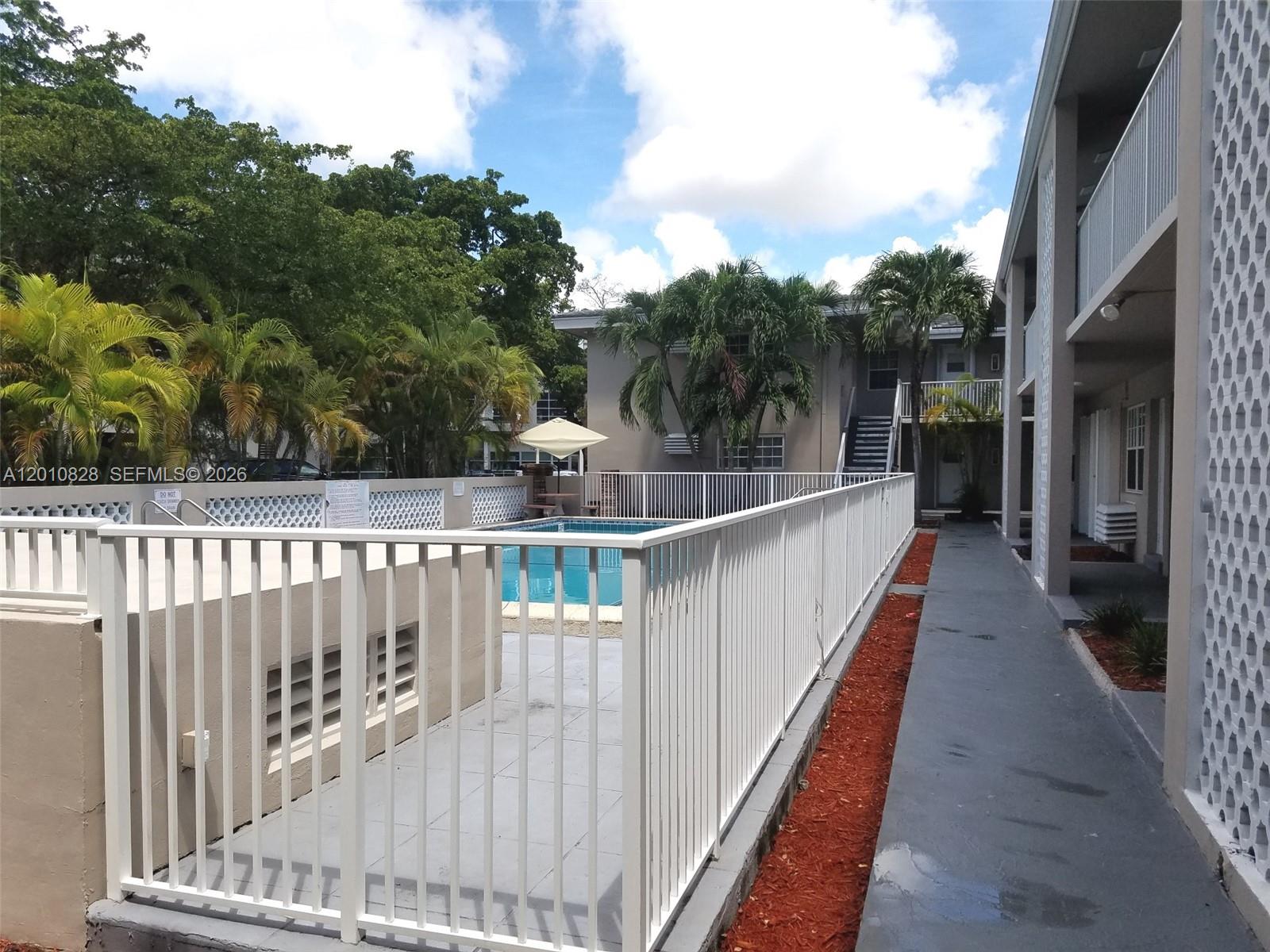 An outdoor swimming pool is enclosed by a white fence next to a residential building — 6565 Santona St # B8, Coral Gables FL 33146, CORAL GABLES, FL