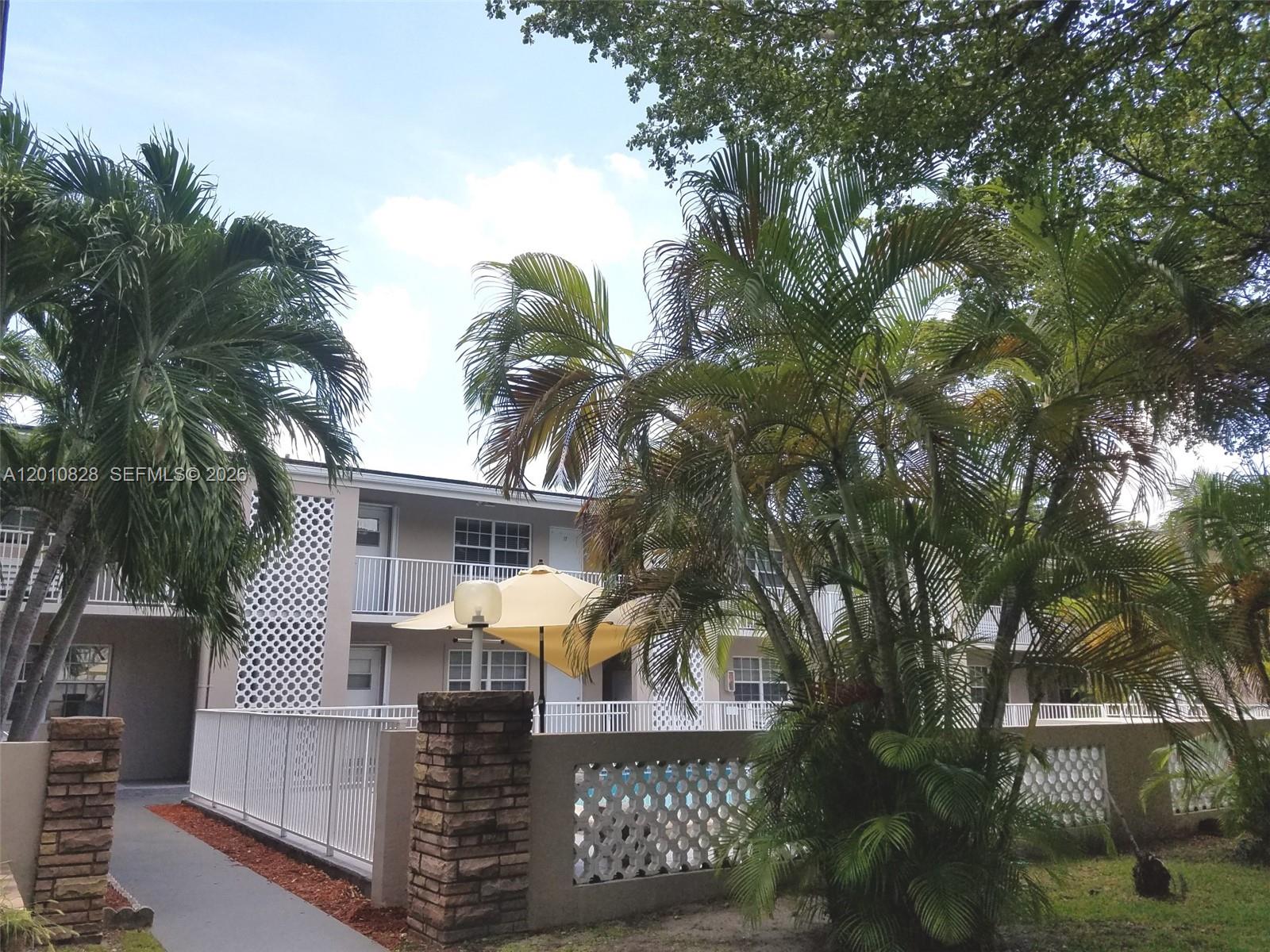 A two-story apartment building features a pool area enclosed by a white fence and palm trees — 6565 Santona St # B8, Coral Gables FL 33146, CORAL GABLES, FL