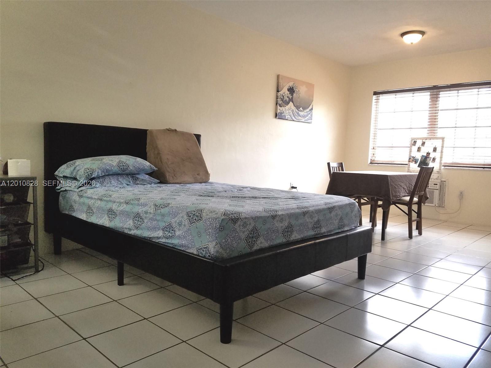 A bedroom features a black bed frame, patterned bedding, and a small dining table nearby — 6565 Santona St # B8, Coral Gables FL 33146, CORAL GABLES, FL