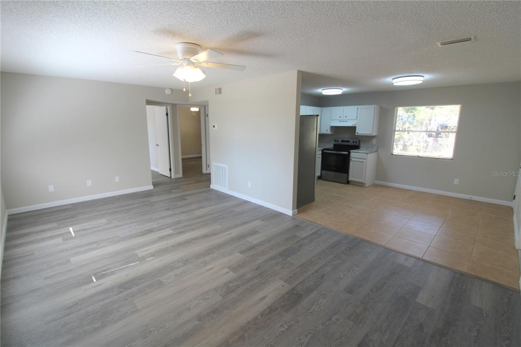 An open-concept living room with wood-look flooring transitions into a tiled kitchen area — 5971 NW 11TH PLACE, OCALA, FL