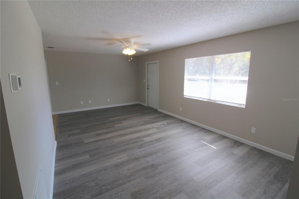 An empty room features gray wood-look flooring, beige walls, a ceiling fan, and a window — 5971 NW 11TH PLACE, OCALA, FL