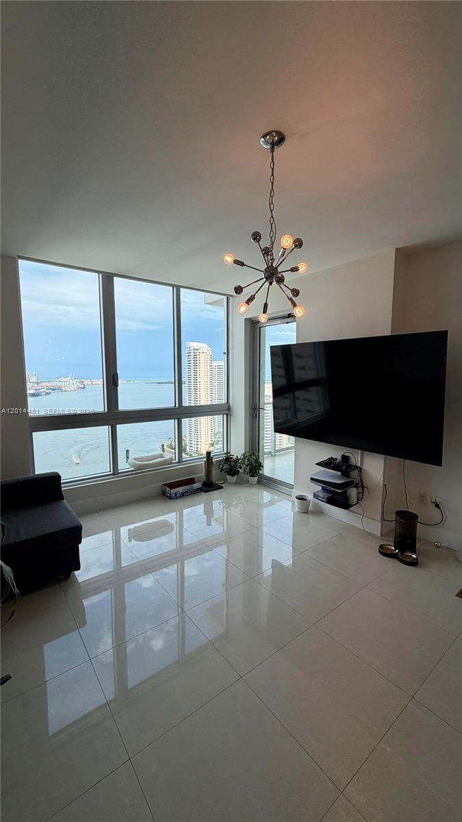 A modern living room features large floor-to-ceiling windows with a water view and tile flooring — 300 S Biscayne Blvd # 3212, Miami FL 33131, MIAMI, FL