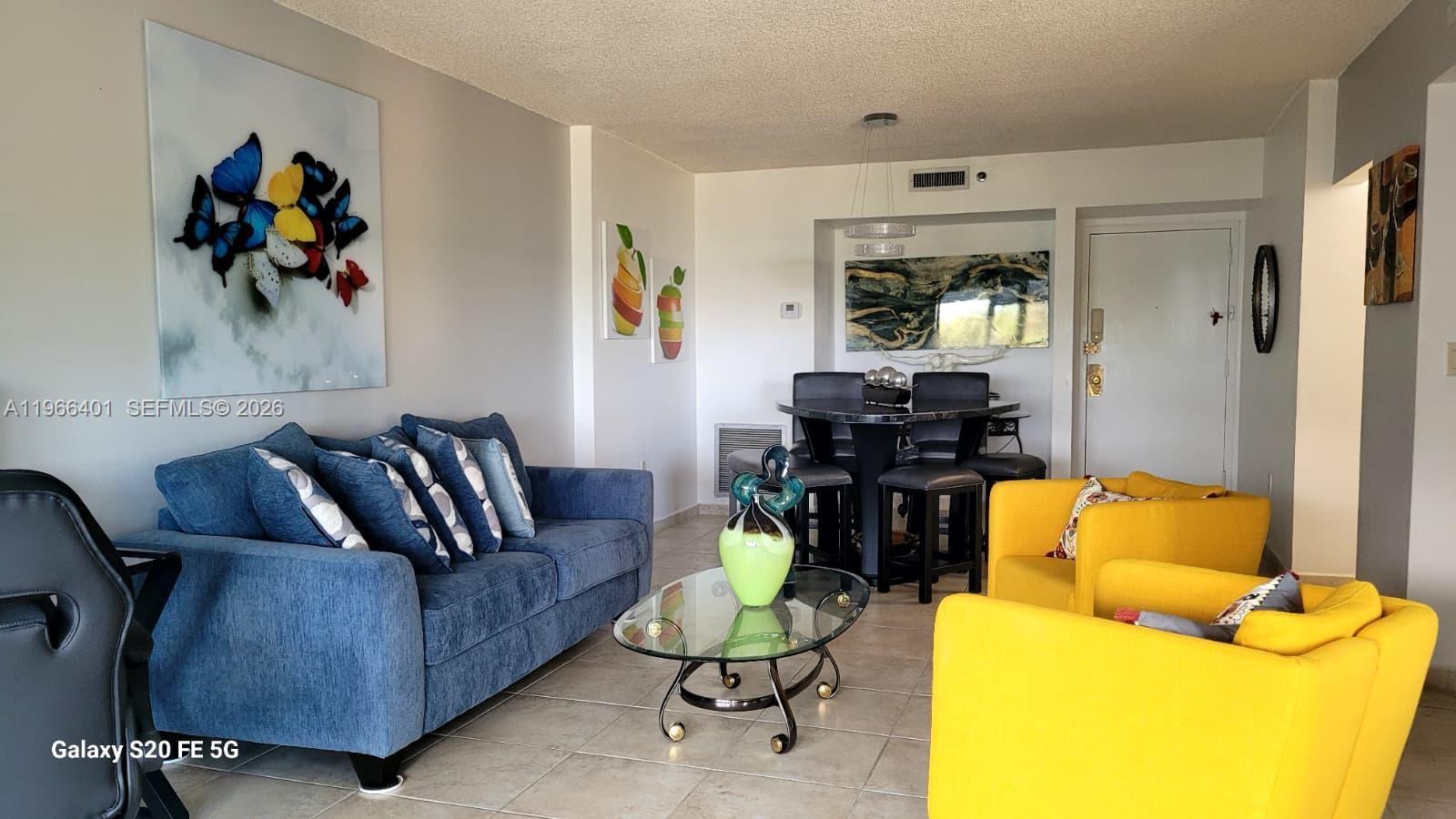 A living and dining area features a blue sofa, yellow armchairs, and a glass coffee table — 4001 Hillcrest Dr # 705, Hollywood FL 33021, HOLLYWOOD, FL