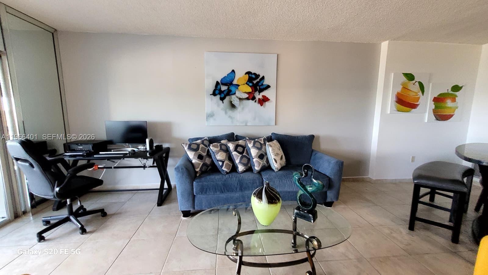 A living room features a blue sofa, a glass coffee table, and a desk area — 4001 Hillcrest Dr # 705, Hollywood FL 33021, HOLLYWOOD, FL