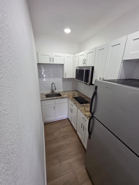 A small kitchen features white cabinets, granite countertops, stainless steel appliances, and wood-look flooring — 1614 N WASHINGTON AVENUE, CLEARWATER, FL