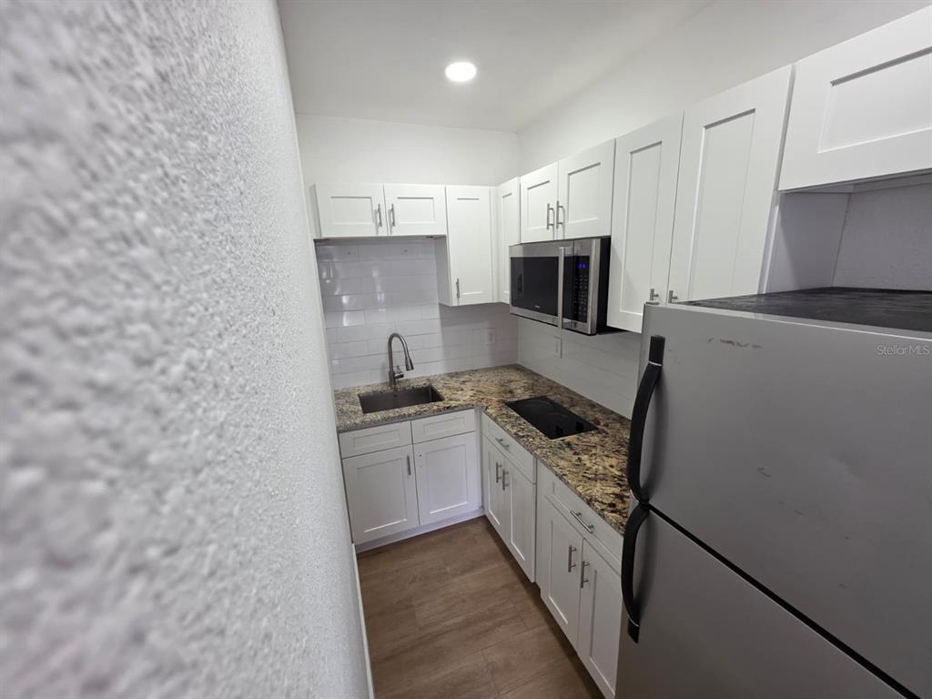 A small kitchen features white cabinets, granite countertops, a stainless steel microwave, and wood-look flooring — 1614 N WASHINGTON AVENUE, CLEARWATER, FL