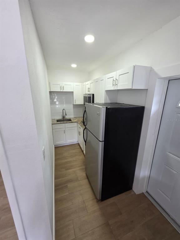 A galley kitchen features white cabinets, stainless steel appliances, and light wood-look flooring — 1614 N WASHINGTON AVENUE, CLEARWATER, FL